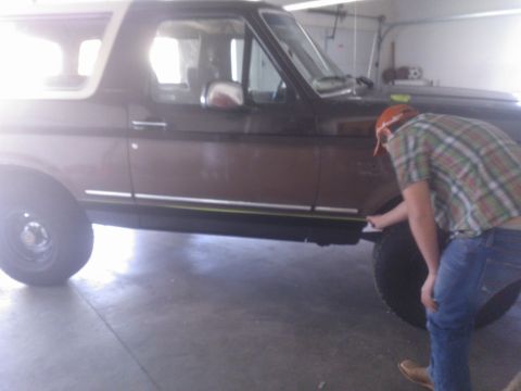 1992 Ford Bronco - A person inspects the side of a brown 1992 Ford Bronco with a white top.