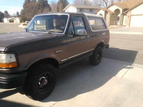 1992 Ford Bronco - A brown 1992 Ford Bronco is parked on a paved surface in front of a residential house.