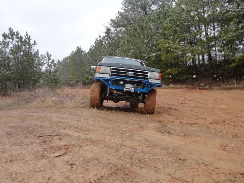 1990 Ford Bronco - A Ford F-Series truck navigates a muddy path with snow falling.