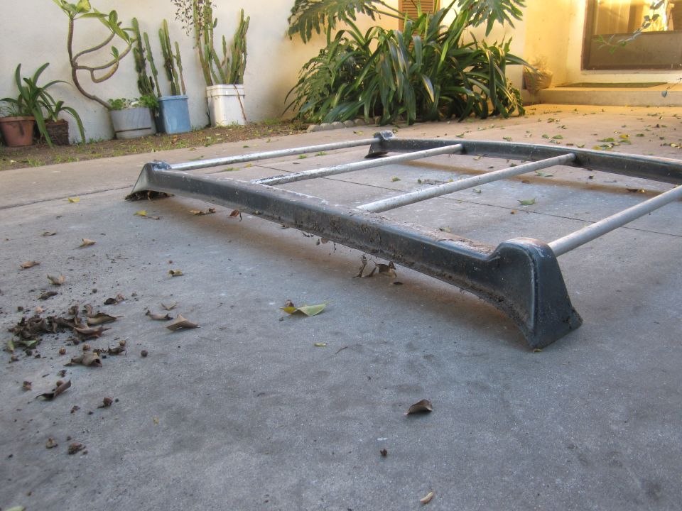 Roof rack assembly lying on concrete patio, with plants in background