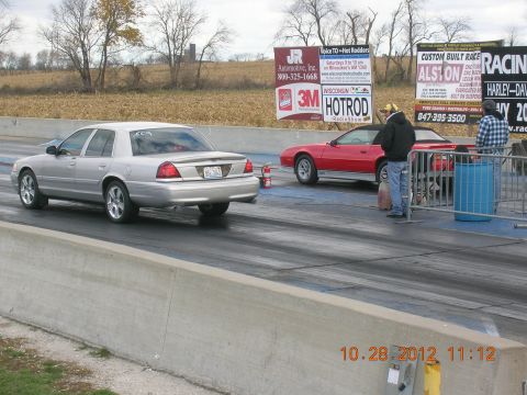 2003 Ford Crown Victoria - Two cars line up on a drag strip, with a silver 2003 Ford Crown Victoria on the left.