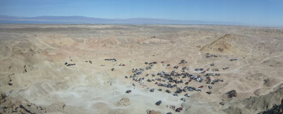 Many off-road vehicles parked in a desert canyon with mountains in the background