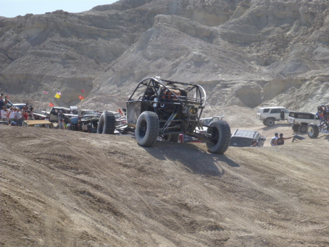 Off-road buggy on dirt hill, other vehicles and people in background