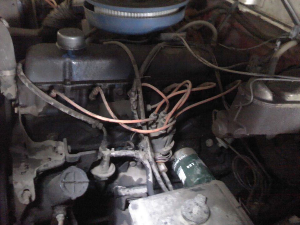 Engine bay with V8 engine block, distributor cap, spark plug wires, and oil filter. Some parts are dusty