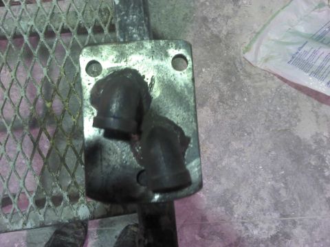 1979 Ford Bronco - A metal plate with two pipe fittings is shown on a concrete surface with a white bag in the background.