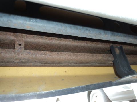 2004 Mercury Grand Marquis - Close-up view of a rusty exhaust pipe and a black bracket on the undercarriage of a vehicle.
