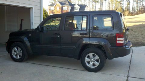 2011 Jeep Liberty - A dark gray Jeep Liberty is parked outside a residential garage on a sunny day.
