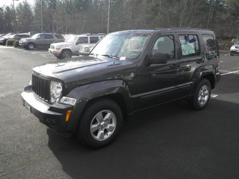 2011 Jeep Liberty - A dark gray Jeep Liberty SUV is parked in a lot with other vehicles, showing a window sticker and a website watermark.