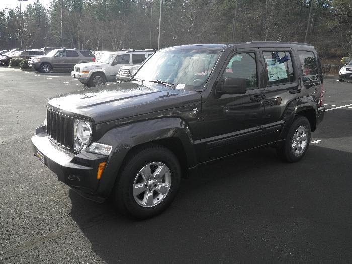 Dark gray Jeep Liberty SUV parked in a lot, front 3/4 view. Visible window sticker and Supermotors.net watermark