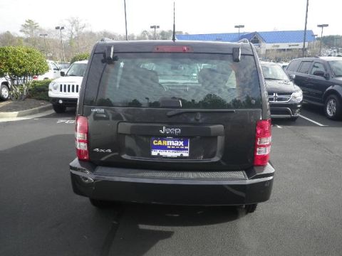 2011 Jeep Liberty - A dark Jeep Liberty is parked in a lot with other vehicles and a building in the background.