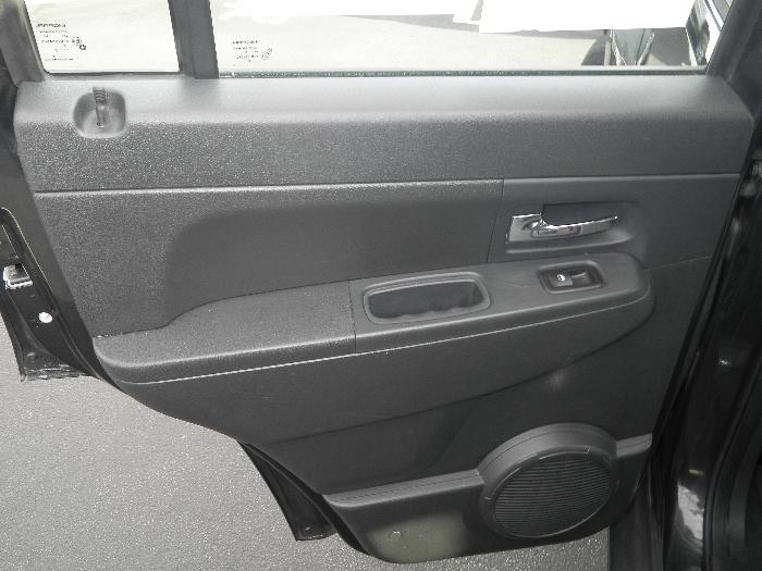 Interior of a black car door showing the armrest, door handle, window control, and speaker grille