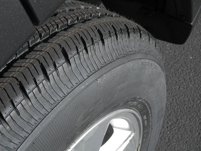 Close-up of a black tire with a silver rim, showing tread detail and a portion of the vehicle's body