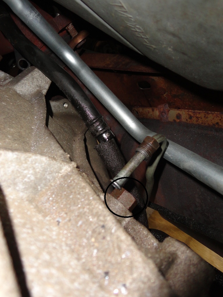 Close-up of a metal fitting on a transmission with a black hose and silver pipe