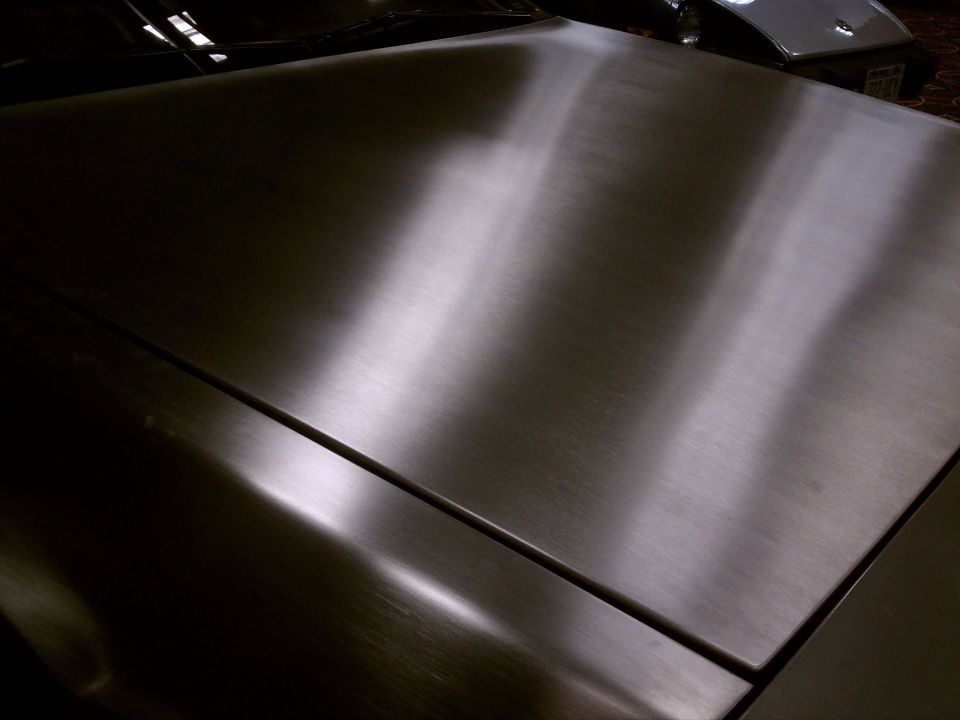 Brushed metal car hood with reflections, another car visible in background