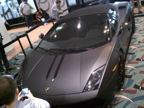1998 Toyota Camry - Matte gray Lamborghini Gallardo with black racing stripes on the hood, seen at an event.