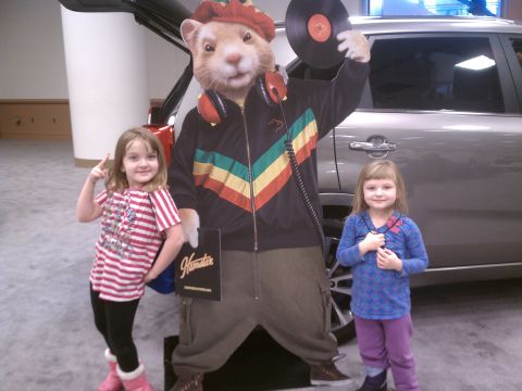 1998 Toyota Camry - A silver SUV is partially visible behind a hamster DJ cutout and two young girls at an event.