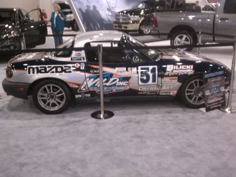 1998 Toyota Camry - A customized Mazda Miata sports car is displayed indoors with various sponsor decals and racing numbers.