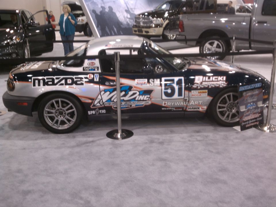 Mazda Miata with racing decals and number 51 on the side. Other vehicles and people are visible in the background