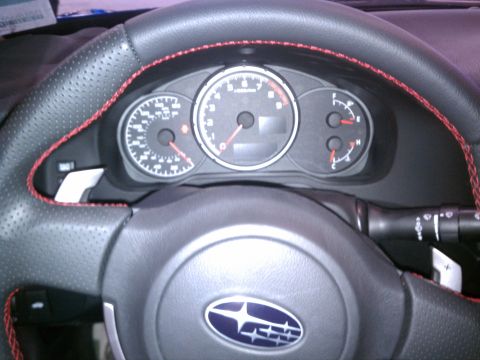 1998 Toyota Camry - The interior of a vehicle shows a steering wheel with red stitching and a Subaru emblem, along with the instrument cluster.