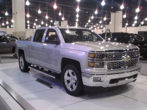 1998 Toyota Camry - A silver Chevrolet Silverado pickup truck is displayed indoors with bright overhead lighting and other vehicles nearby.