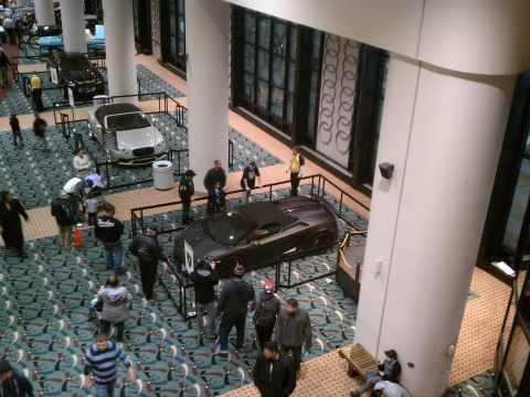1998 Toyota Camry - A dark sports car is displayed at an auto show, with people observing.