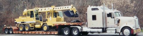 2001 Ford F-350 - A large yellow crane is transported on a flatbed trailer pulled by a semi-truck.