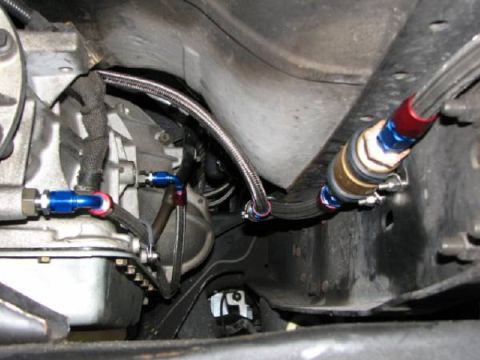 1990 Ford Bronco - Close-up of braided fuel lines connected to a vehicle's transmission system.