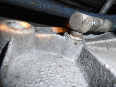 1990 Ford Bronco - A close-up view of a metal component, likely from a vehicle's transmission, with a bolted hose fitting attached.