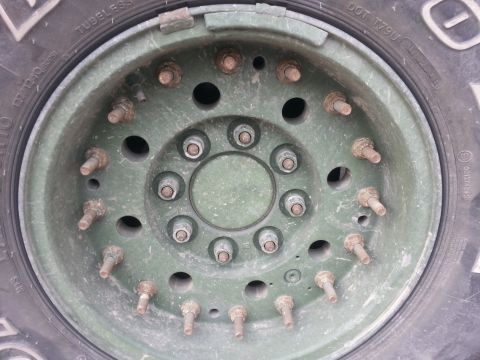 1989 Ford Bronco - Close-up of a heavy-duty green military truck wheel, showing its robust construction with numerous lug nuts and studs.