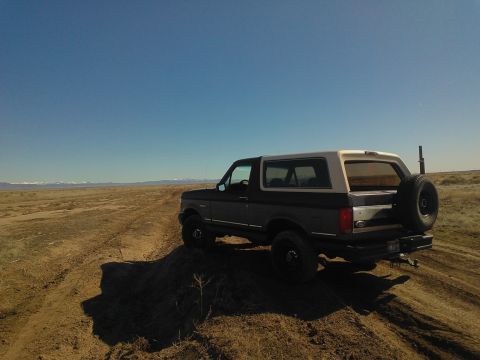 1992 Ford Bronco - Ford Bronco navigates a dusty off-road path under a clear blue sky.