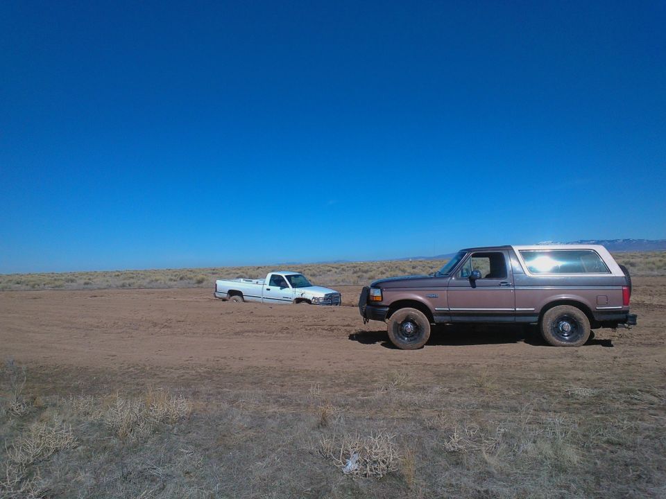 1992 Ford Bronco parked on dirt, white truck stuck in background