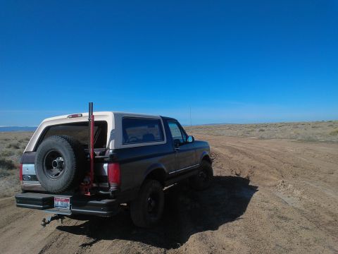 1992 Ford Bronco - A Ford Bronco navigates a dusty, off-road trail under a clear blue sky.