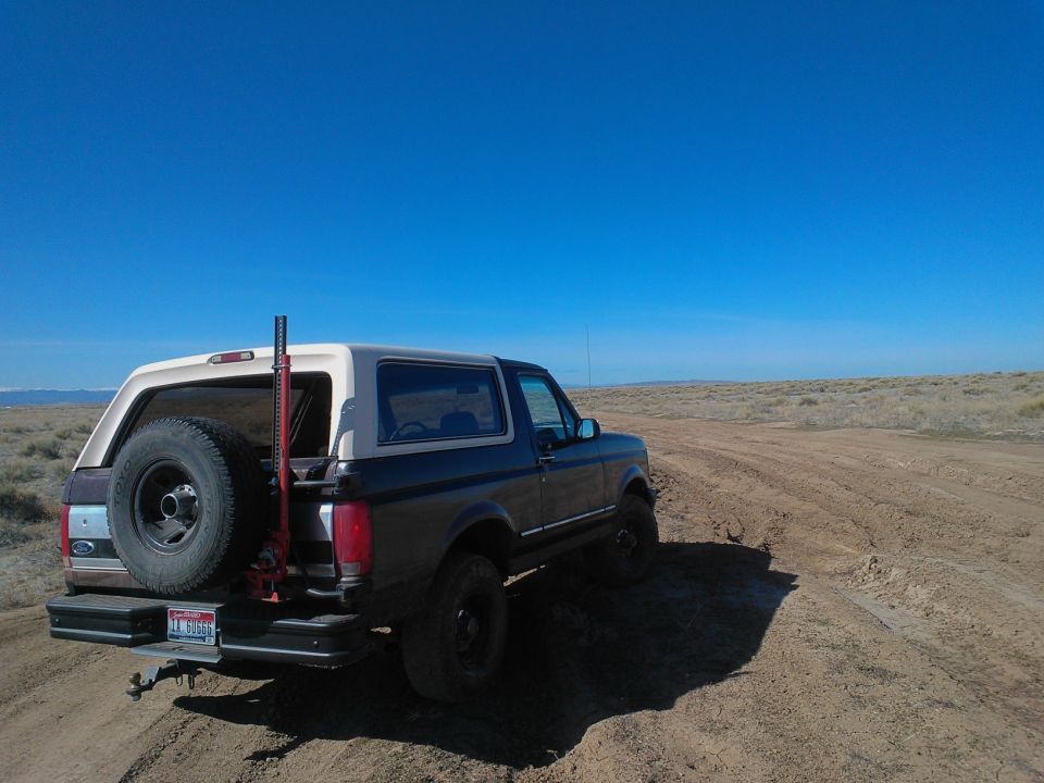 Dark blue and tan Ford Bronco with a spare tire on the back, driving on a dirt road