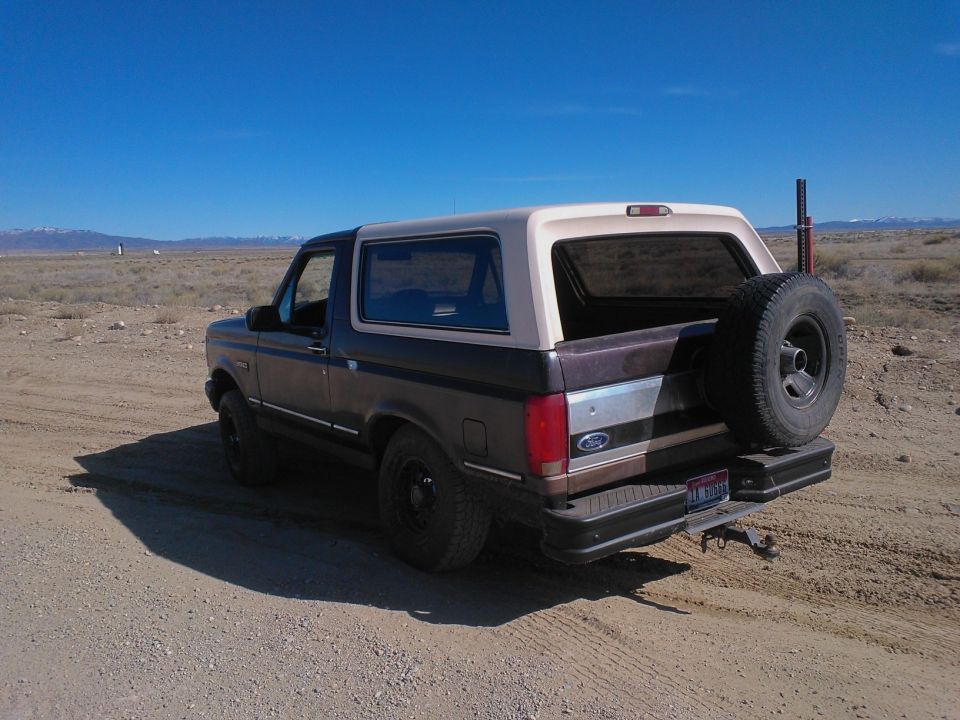 1992 Ford Bronco parked on dirt road with spare tire on rear door. Desert scenery and clear blue sky