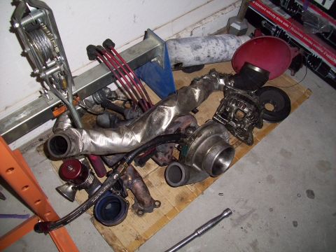 1995 Ford Probe - Various automotive engine parts, including a turbocharger and exhaust manifold, are laid out on a wooden pallet.