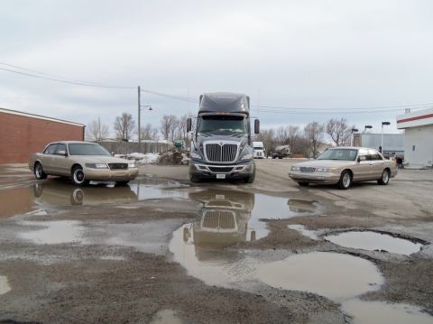 2000 Mercury Grand Marquis - Two 2000 Mercury Grand Marquis sedans and a semi-truck are parked in a lot with large puddles.