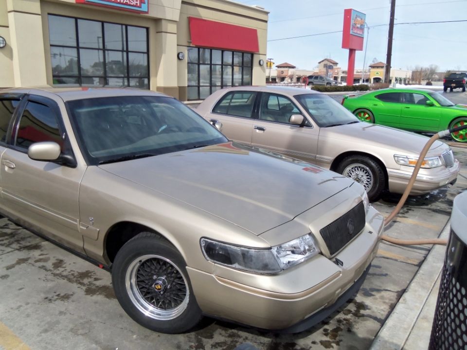 Gold Mercury Grand Marquis parked next to a tan one and a green car at a car wash