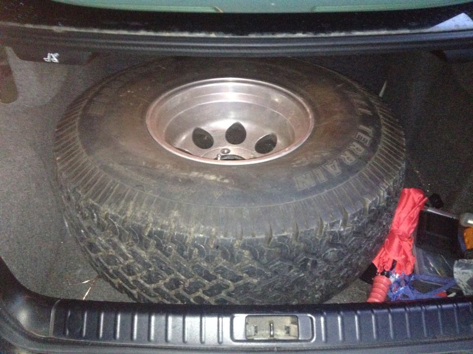 Spare tire with aluminum rim in a car trunk, next to a red emergency kit
