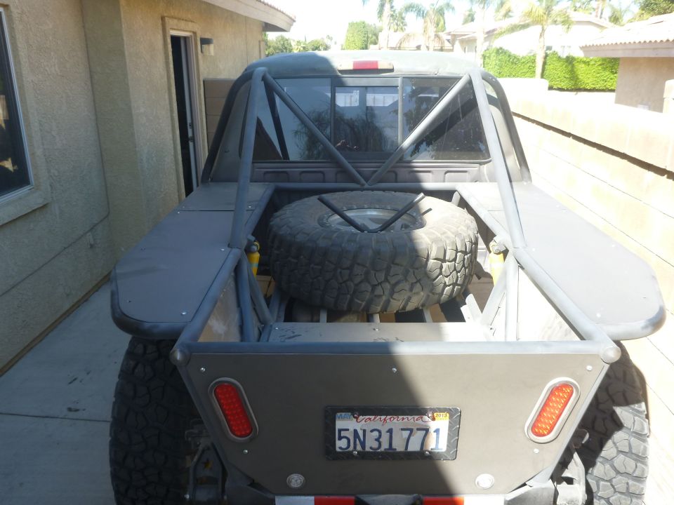 Rear view of modified pickup truck bed with spare tire, roll cage, and California license plate 5N31771