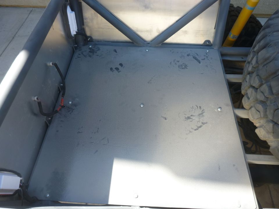 Inside of a custom off-road vehicle, showing the floor pan, roll cage, and a spare tire