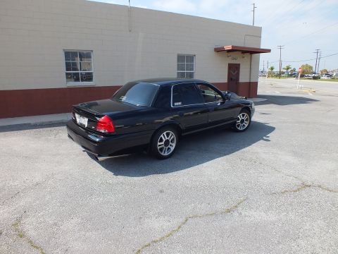 2003 Ford Crown Victoria - Rear three-quarter view of a black full-size sedan on silver wheels in an open lot.