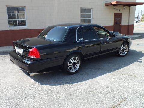 2003 Ford Crown Victoria - Black full-size sedan from the rear quarter, dual chrome exhaust tips and silver wheels visible.