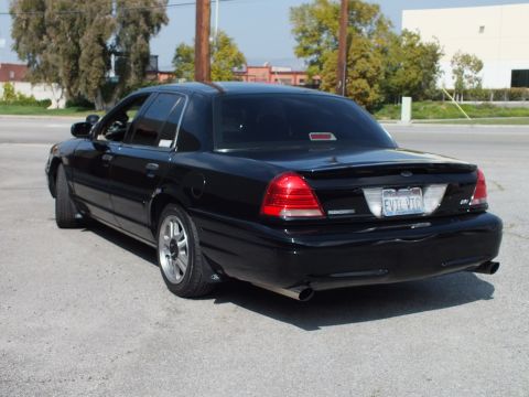 2003 Ford Crown Victoria - Rear three-quarter view of a black sedan with EVIL VIC California plate and dual exhaust.