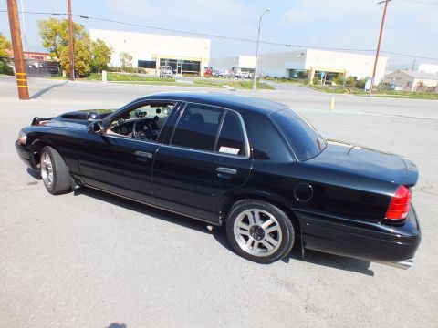2003 Ford Crown Victoria - Black full-size sedan with hood raised, viewed from the left rear quarter on silver wheels.