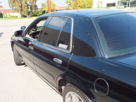 2003 Ford Crown Victoria - Rear-door and quarter window of a black sedan, decal in glass; a stop sign sits behind