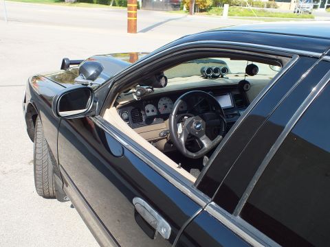 2003 Ford Crown Victoria - Through the door glass: tan dashboard, white instrument cluster and steering wheel of a black sedan