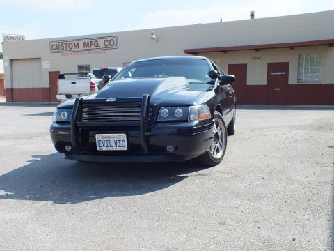 2003 Ford Crown Victoria - Front of a blacked-out sedan, EVIL VIC California plate and push bumper, by an industrial building