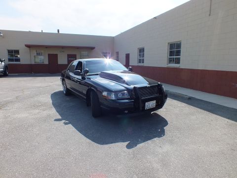 2003 Ford Crown Victoria - Three-quarter front of a black sedan with brush guard parked on pavement by a warehouse