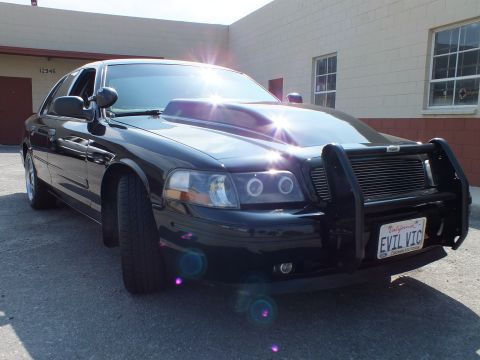 2003 Ford Crown Victoria - Sun-flared shot of a black Crown Victoria-style sedan's nose with push bumper and EVIL VIC plate