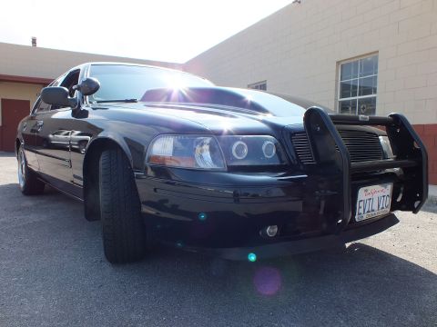 2003 Ford Crown Victoria - Ground-level angle of a black sedan nose showing halo headlights, brush guard and EVIL VIC plate